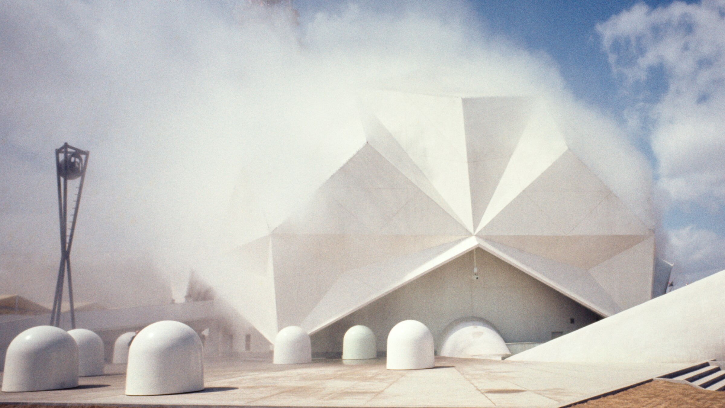 Fog envelops the faceted Pepsi-Cola Pavilion at Osaka Expo ’70, with white kinetic Floats in front and a dark light tower at left.