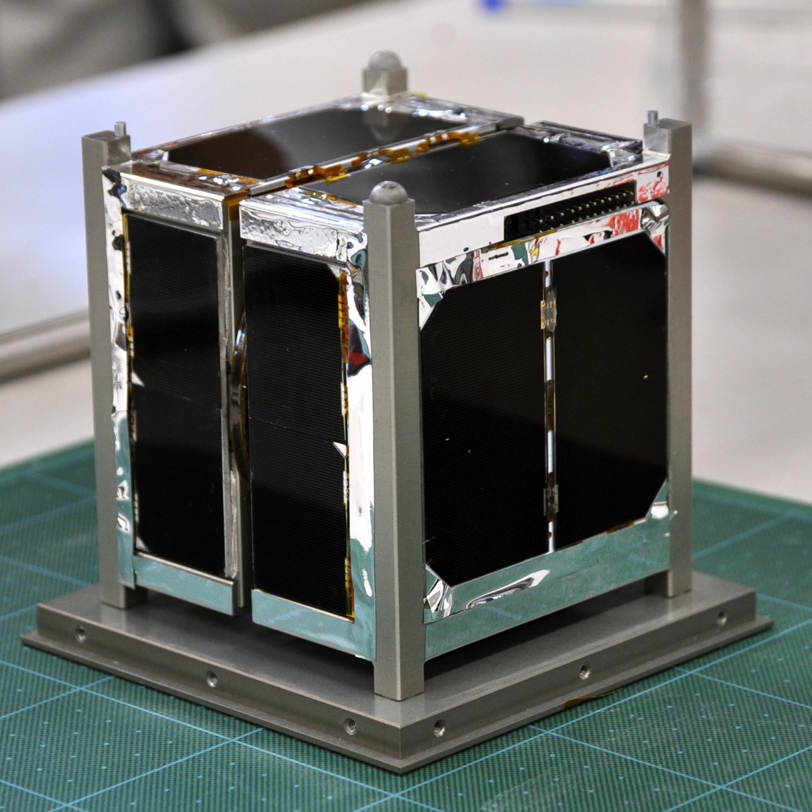ARTSAT1: INVADER CubeSat flight hardware on a green work mat, with black solar panels inside its square metal frame.