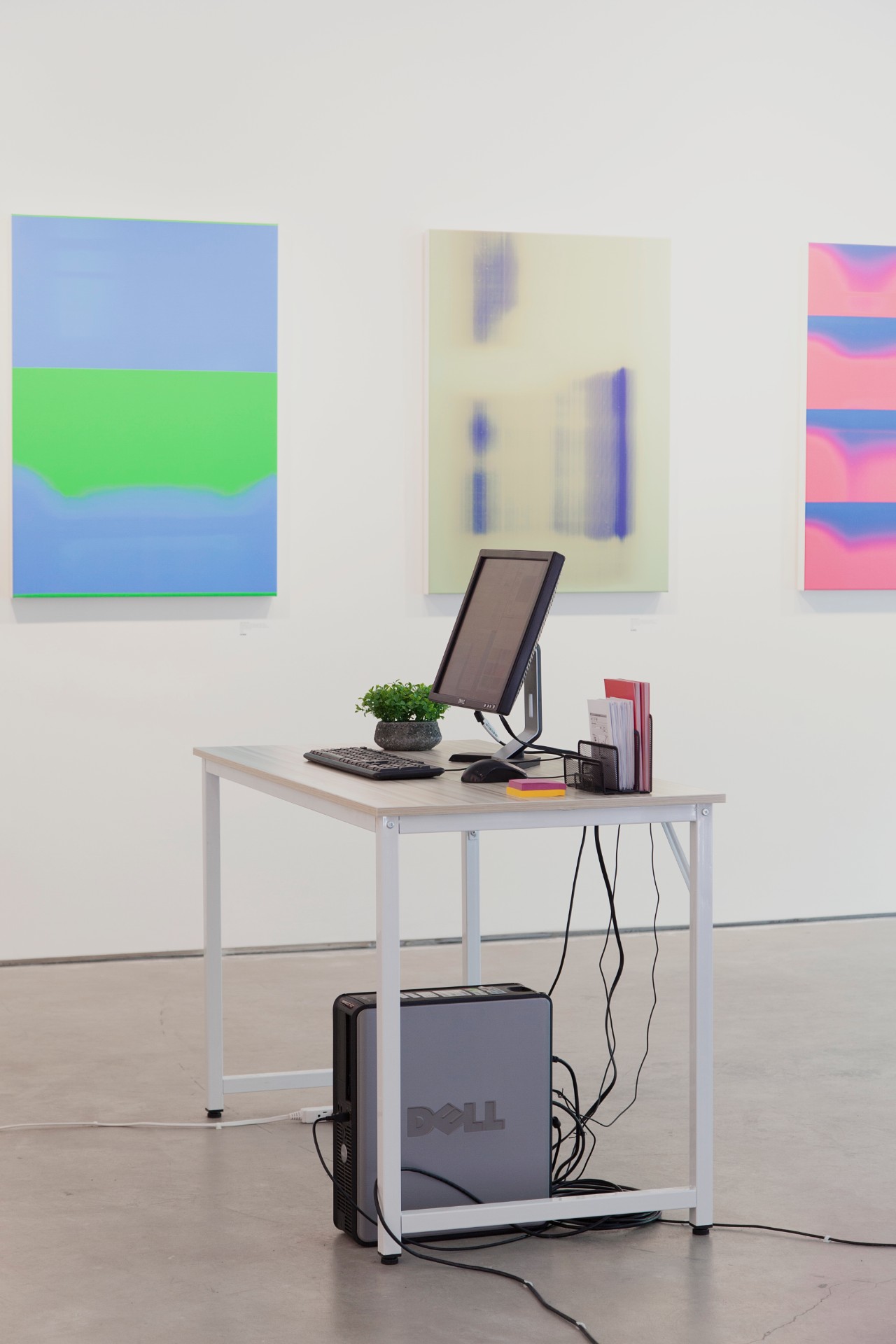 Installation view of the work: machine-generated images hung as prints on the gallery wall behind the desktop computer that runs the scanning system.