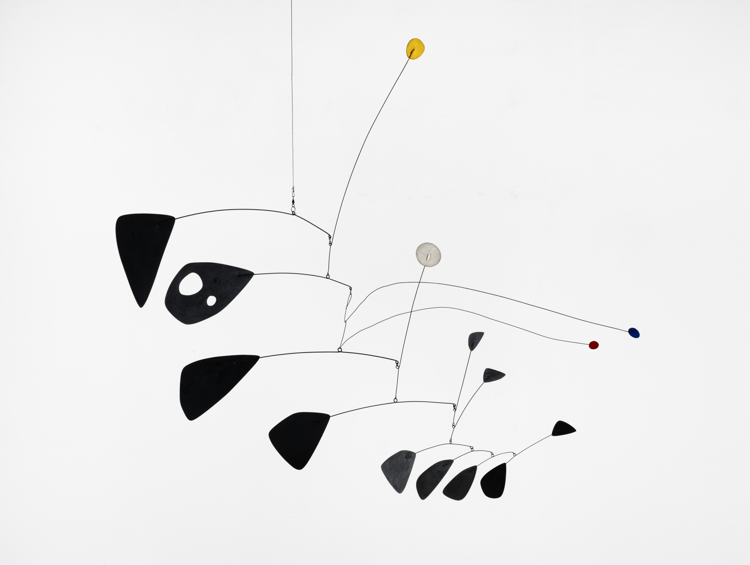 A suspended Calder mobile with black metal leaves and small yellow, white, red and blue discs, isolated against a pale background.