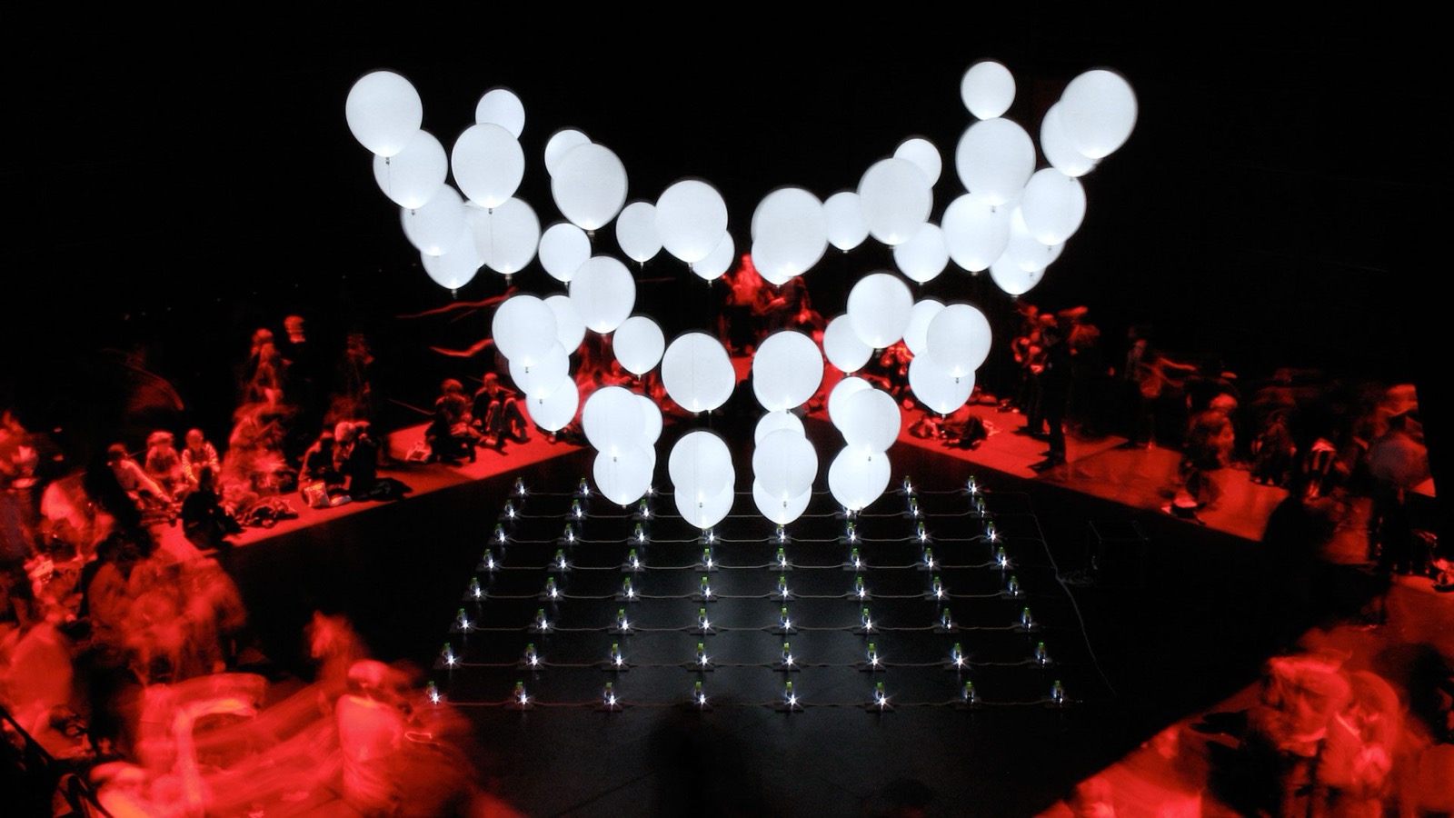 An installation view of ATOM, with the helium balloons lit from within by LEDs and suspended in a computer-controlled three-dimensional matrix above the audience.