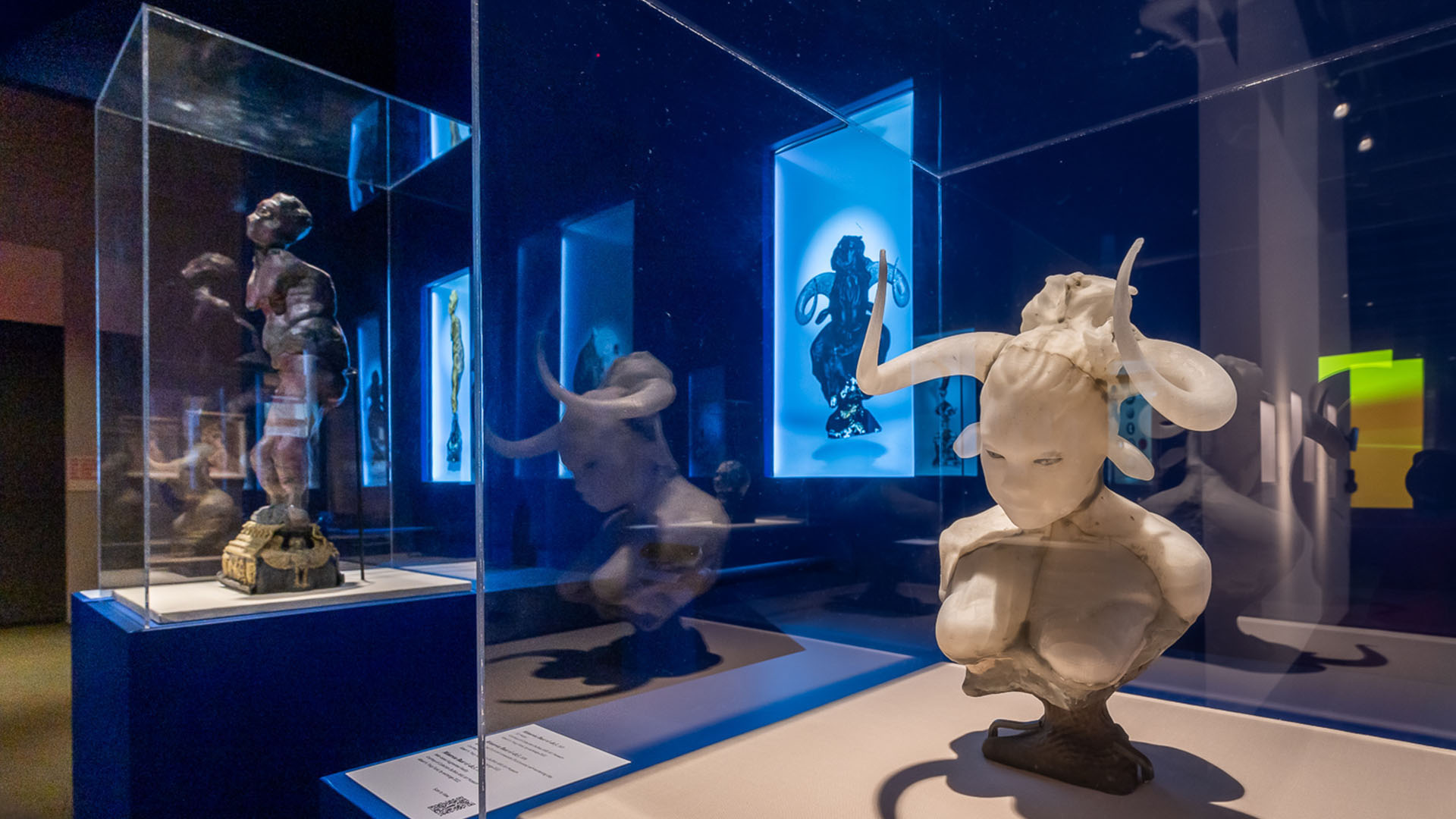 Auriea Harvey’s sculptural figures in glass cases, with digital works glowing blue behind them in the MoMI exhibition.