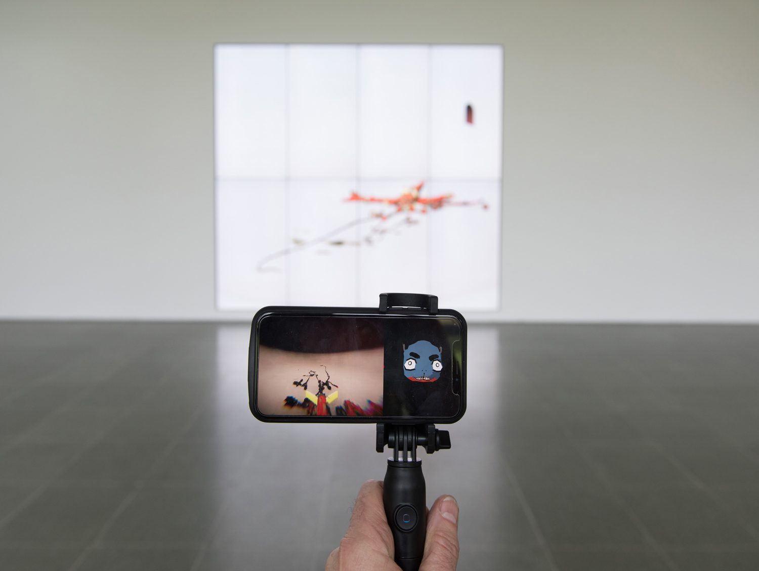 Installation view of BOB at the Serpentine Galleries: the projected creature on the gallery wall with a visitor viewing it through the accompanying phone app on a handheld mount.