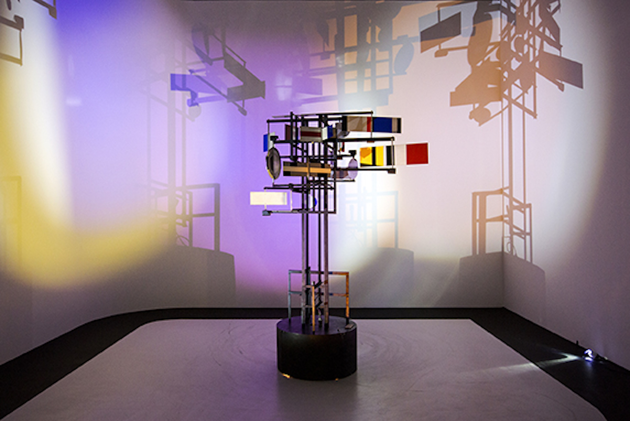 CYSP 1 kinetic sculpture with colored panels casting large shadows across illuminated gallery walls.