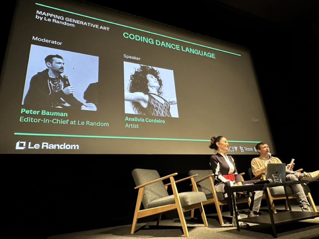 Analívia Cordeiro and Peter Bauman sit on stage beneath a Coding Dance Language presentation screen.