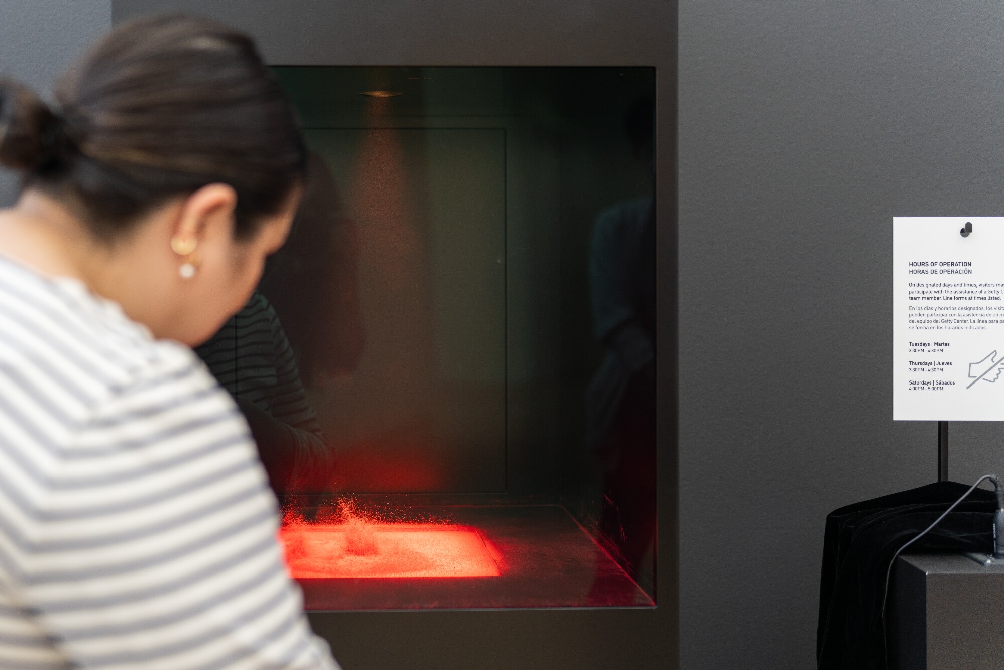 A visitor watches bright red powder move inside a glass-fronted box responding to a heartbeat.