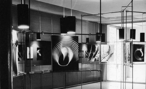 Black-and-white view of suspended display panels containing abstract photographic patterns and oscillographic forms.
