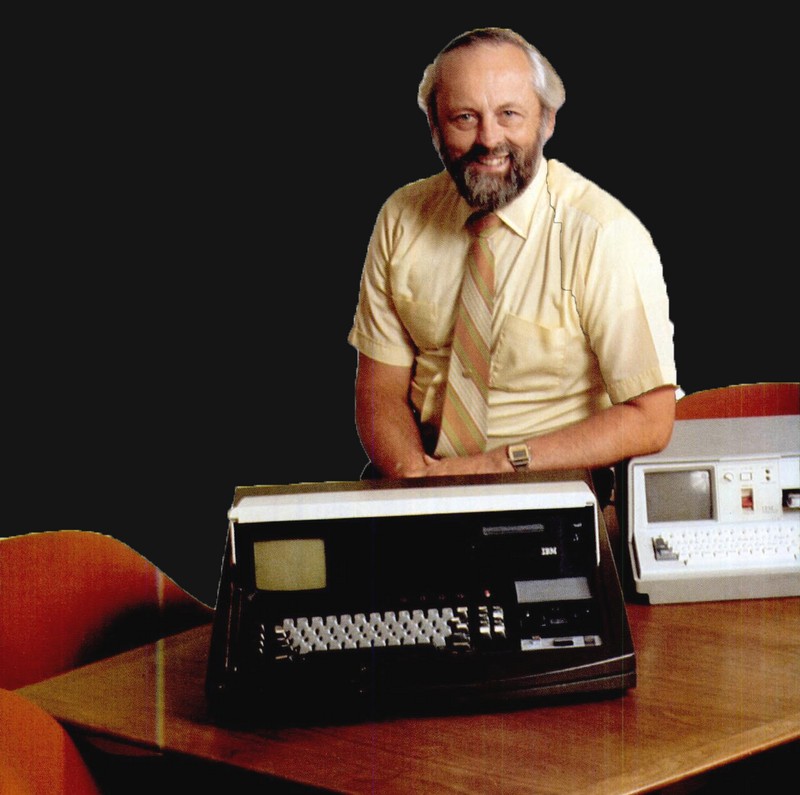 Paul Friedl seated behind the black SCAMP portable-computer prototype, beside a later white IBM computer.