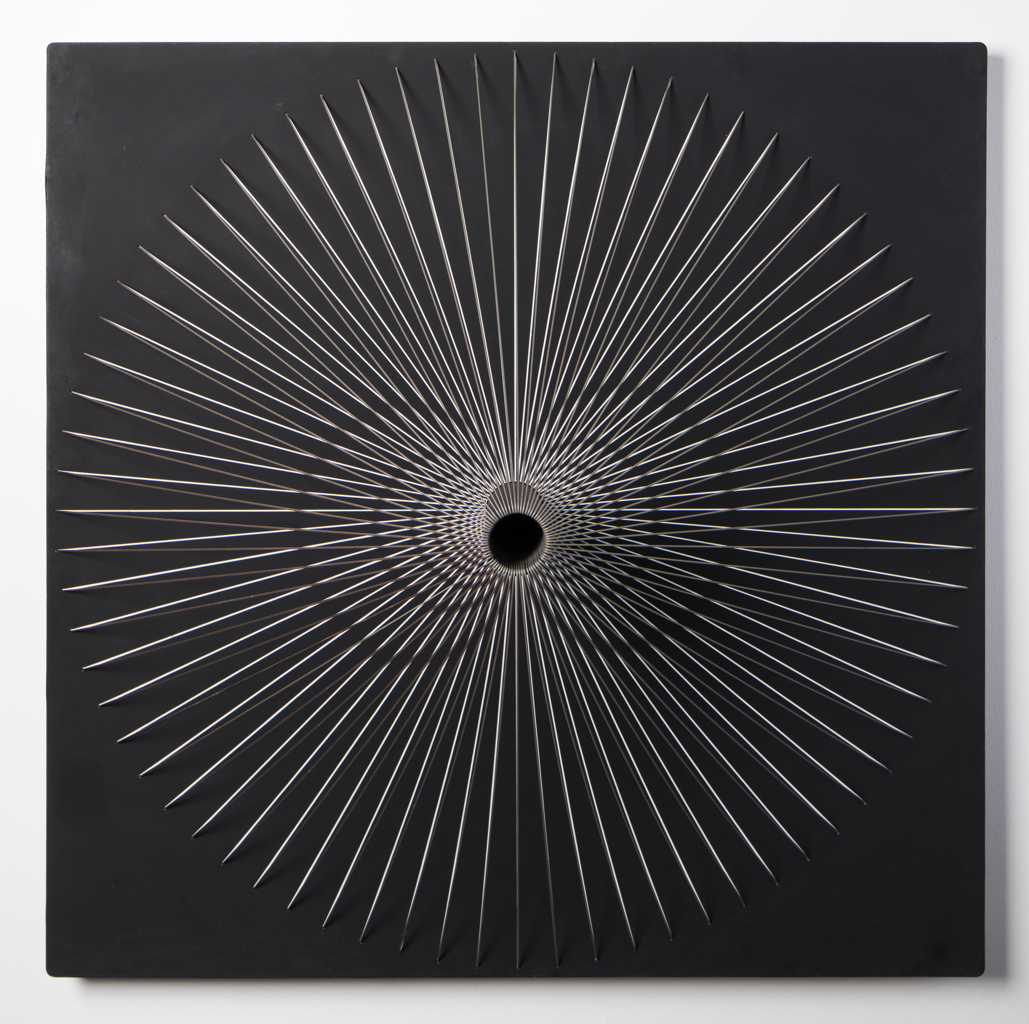 Thin pale lines radiate and cross around a dark central opening on a square black wall piece, producing dense optical interference patterns.