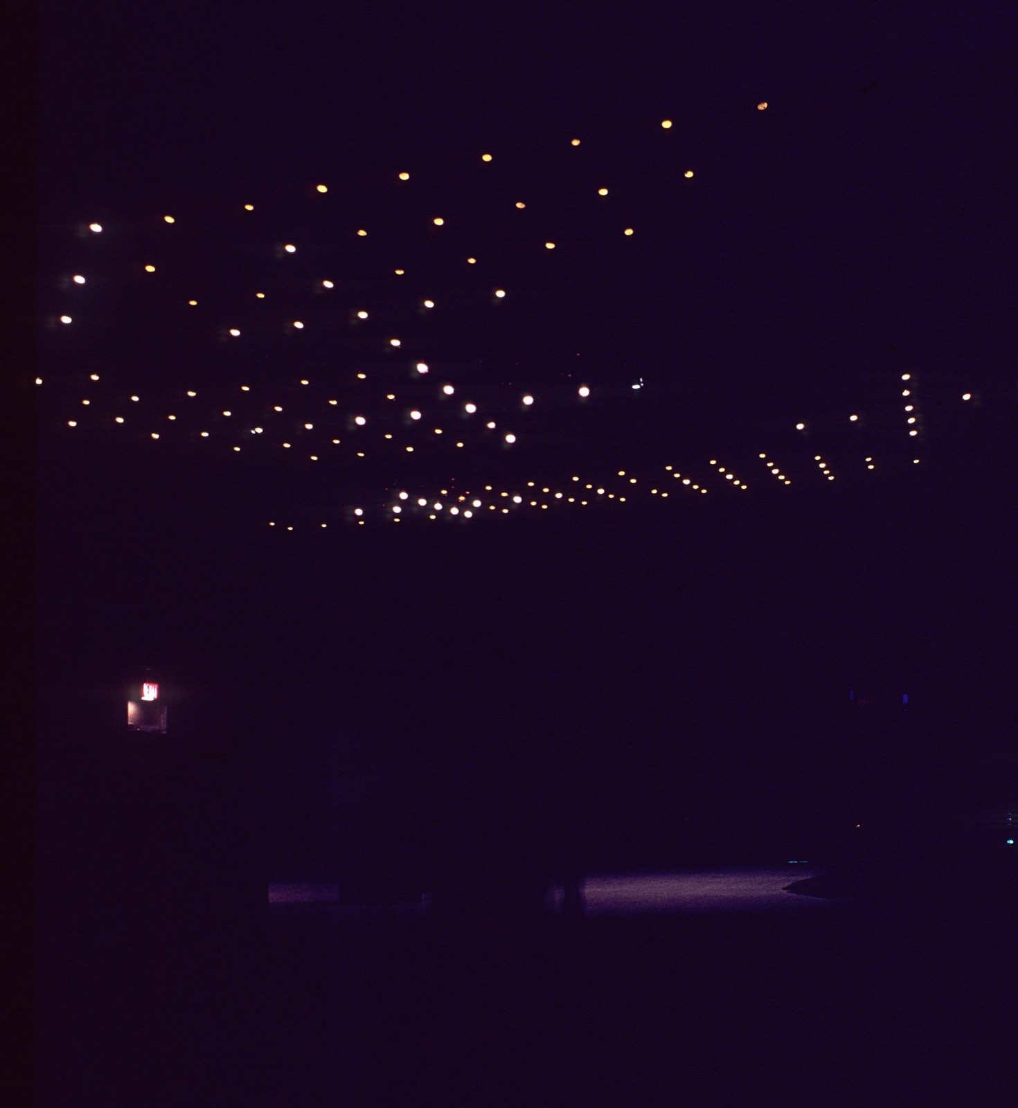 An installation view of James Seawright's Network III (1971): the overhead grid of lamps in a darkened gallery, lit in the shifting patterns triggered by visitors standing on the floor sensors below.