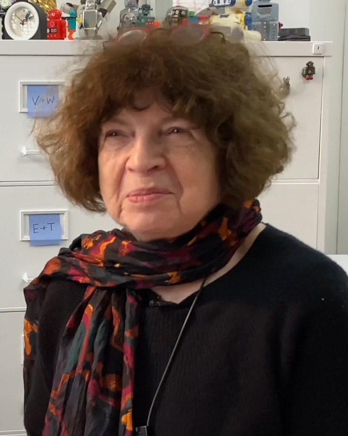 Jasia Reichardt photographed in London in February 2022, seated in front of a filing cabinet topped with a row of toy robots; this is a recent portrait, not a photograph from the 1970s.