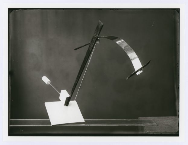 Black-and-white photograph of a Bauhaus balance construction with a curved metal support and suspended circular and rectangular weights.