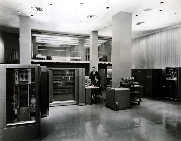 IBM 704 computer room with console, tape drives, storage cabinets and operators.
