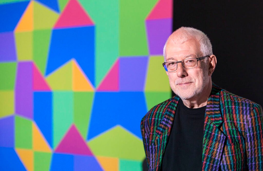 A photographic portrait of the artist and writer Paul Brown, author of 'Beyond Art', standing in front of one of his own multicoloured tiling works.