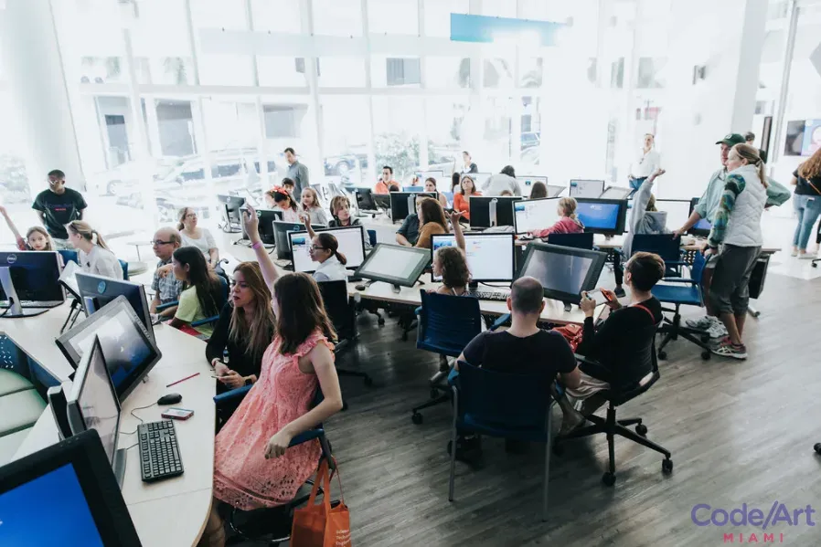 A bright computer classroom filled with children and adults making creative work at desktop computers.