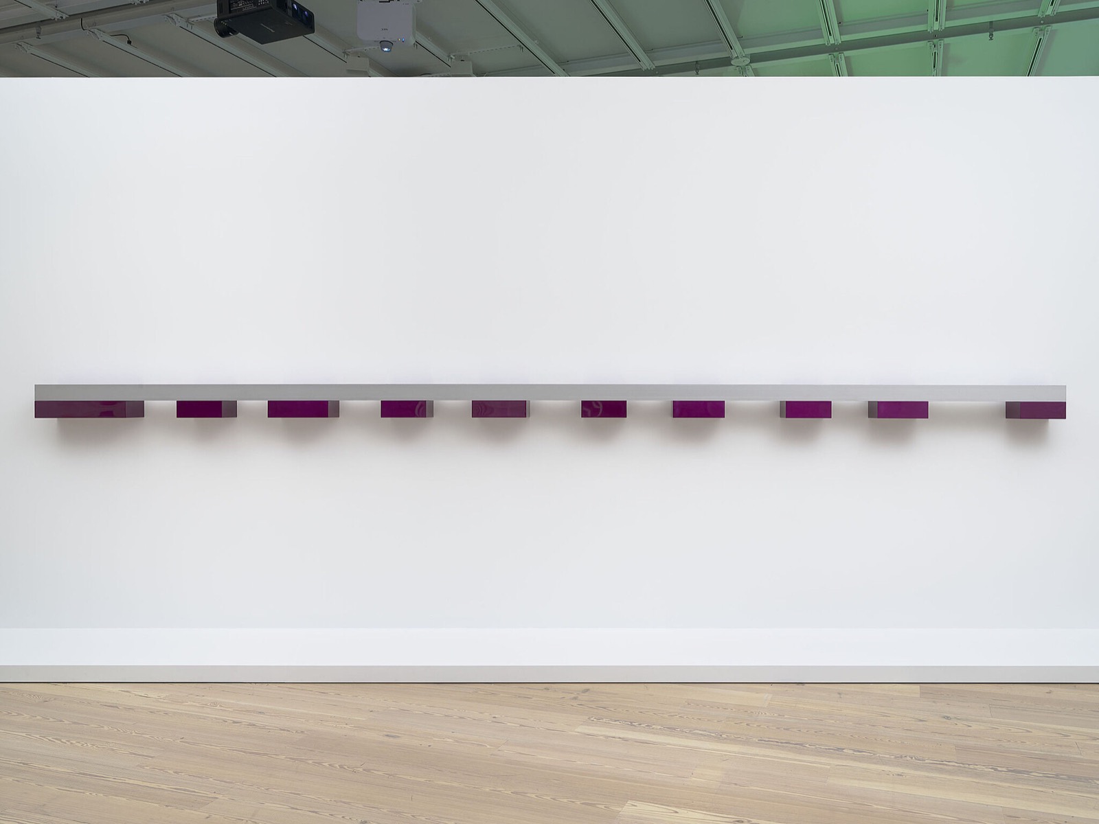 An installation view from the Whitney's Programmed, showing a row of small magenta-lit works mounted along a shelf on the gallery wall.