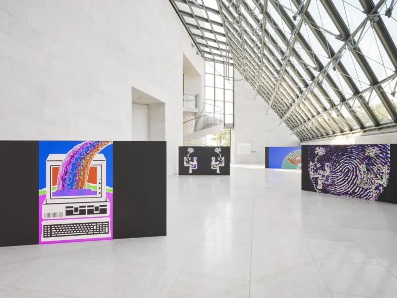 An installation view rather than a single work: the exhibition installed under the glass roof of Mudam's Grand Hall, with a pink-and-blue computer-graphic panel of a monitor and rainbow in the foreground and further screen-print panels, including a fingerprint image, receding down the hall.
