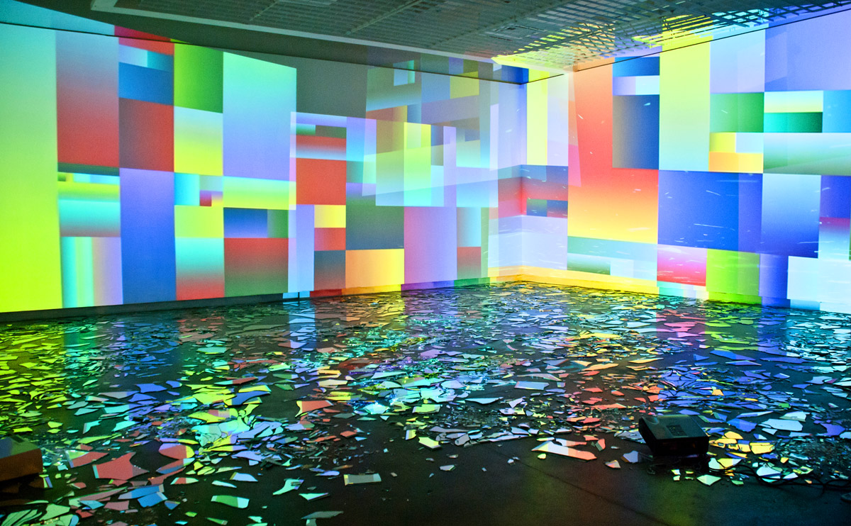 Multicolored rectangular projections cover the walls of Into Time with mirrors, reflected in scattered mirror fragments across the floor.