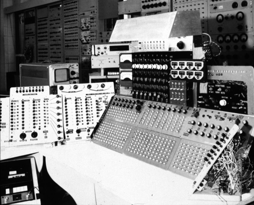 Electronium console with dense rows of knobs and switches, several open circuit panels and a central control surface.