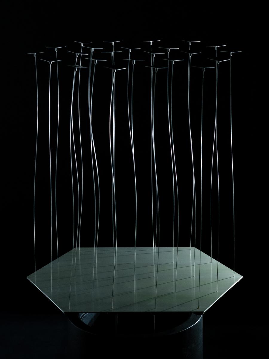 Thin metal rods rise from a square reflective base in a dark space, each ending in a small square plate seen edge-on; several rods appear curved or doubled in motion.
