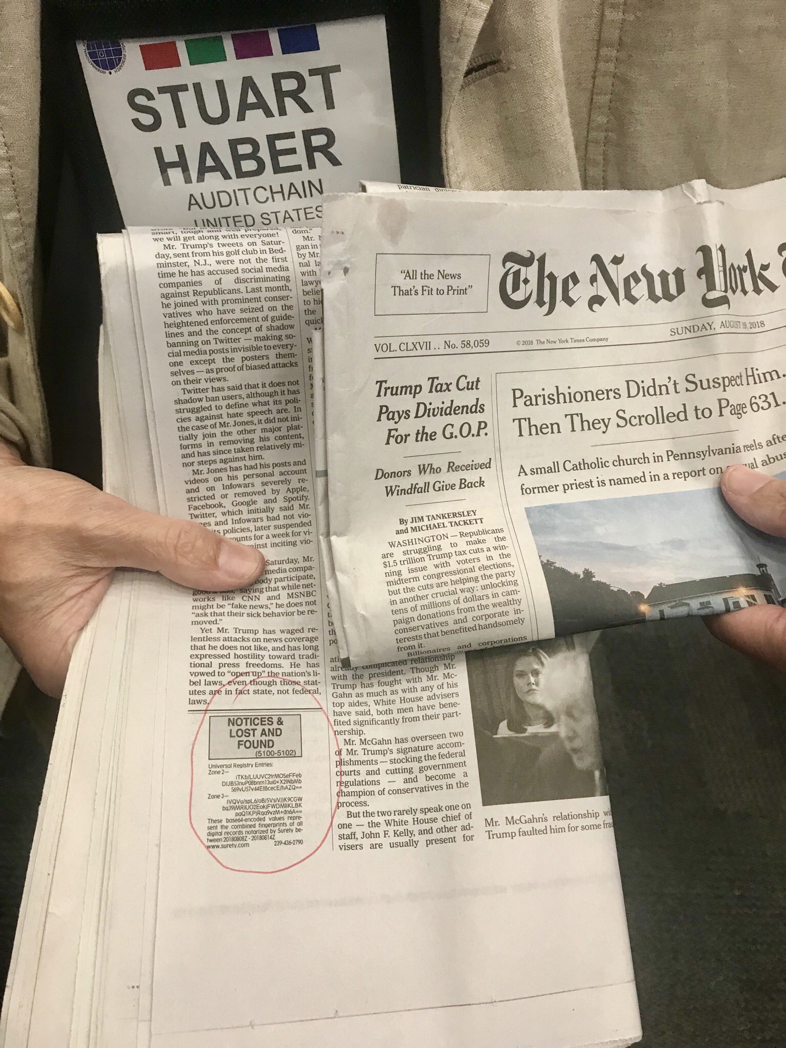 A Surety 'Universal Registry Entries' notice circled in red in the classified pages of The New York Times of 19 August 2018 — the weekly published hash chain that has run since 1995 on Haber and Stornetta's scheme. Stuart Haber's conference badge is visible behind the newspaper.