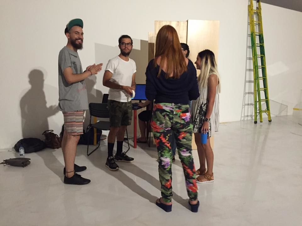 Five people gather in a white gallery during installation, with a ladder and equipment beside them.