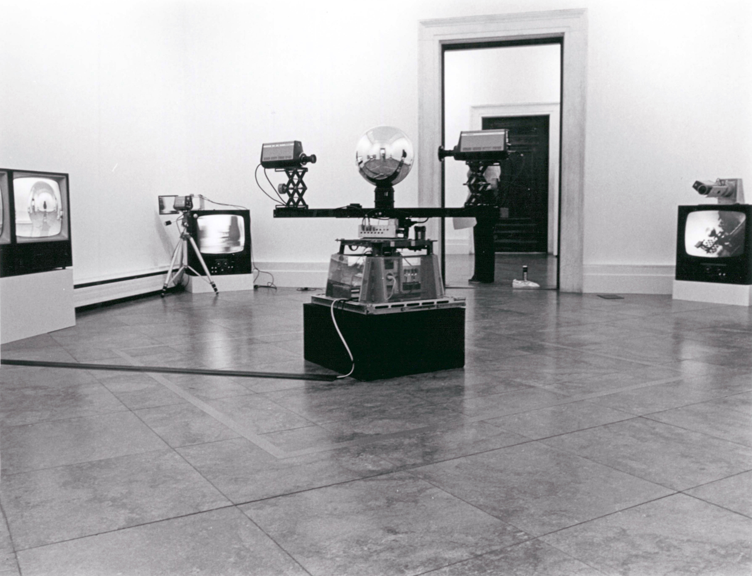 Video cameras face a reflective sphere in a gallery installation, with CRT monitors arranged around the room.