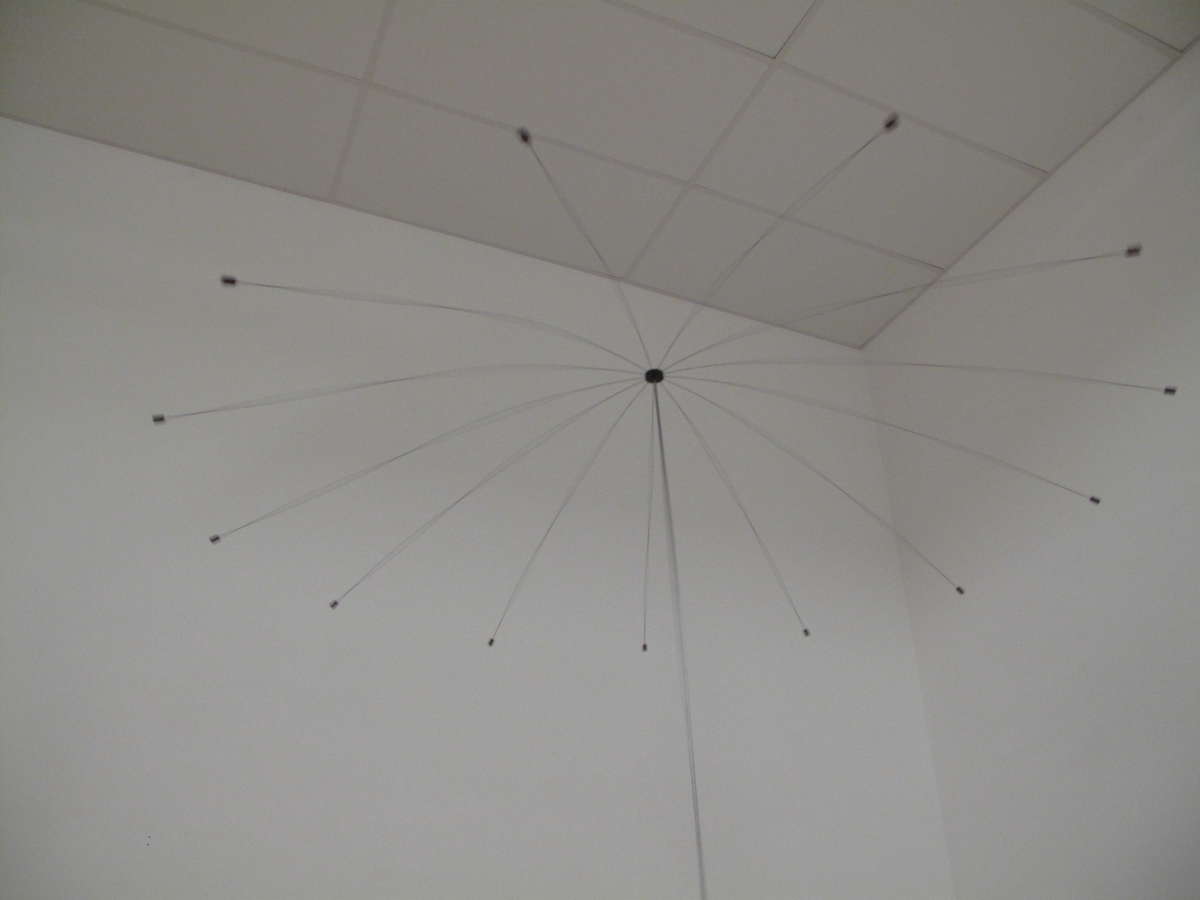 A detail of Wen-Ying Tsai's Umbrella (1971) installed at Tate Modern, looking up at the central crown from which thirteen fine stainless-steel rods radiate, each weighted at its tip.