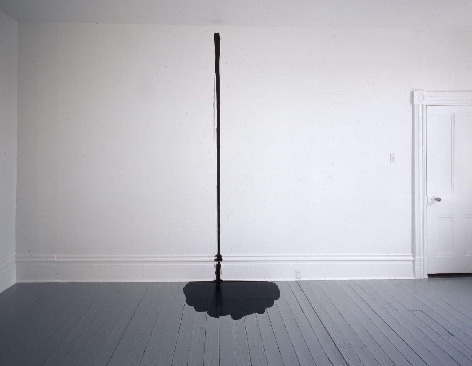 A gallon of black industrial enamel poured down a white gallery wall and pooling on the floor, in the Mattress Factory's installation of William Anastasi's poured-enamel work.