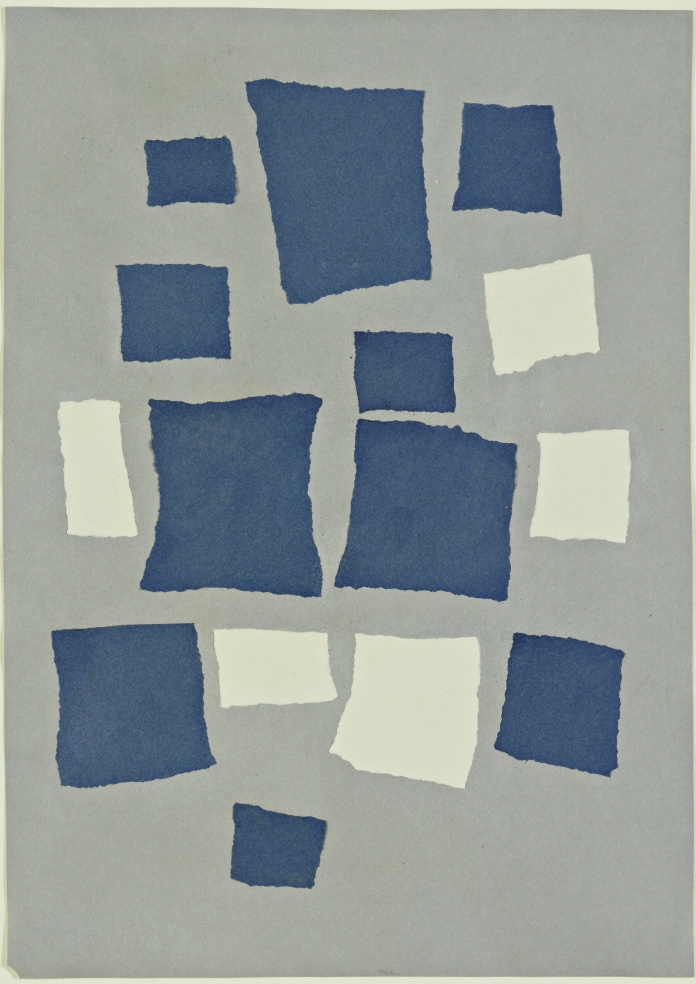 Torn blue and ivory paper squares arranged loosely across a warm gray sheet, with textured torn edges visible.