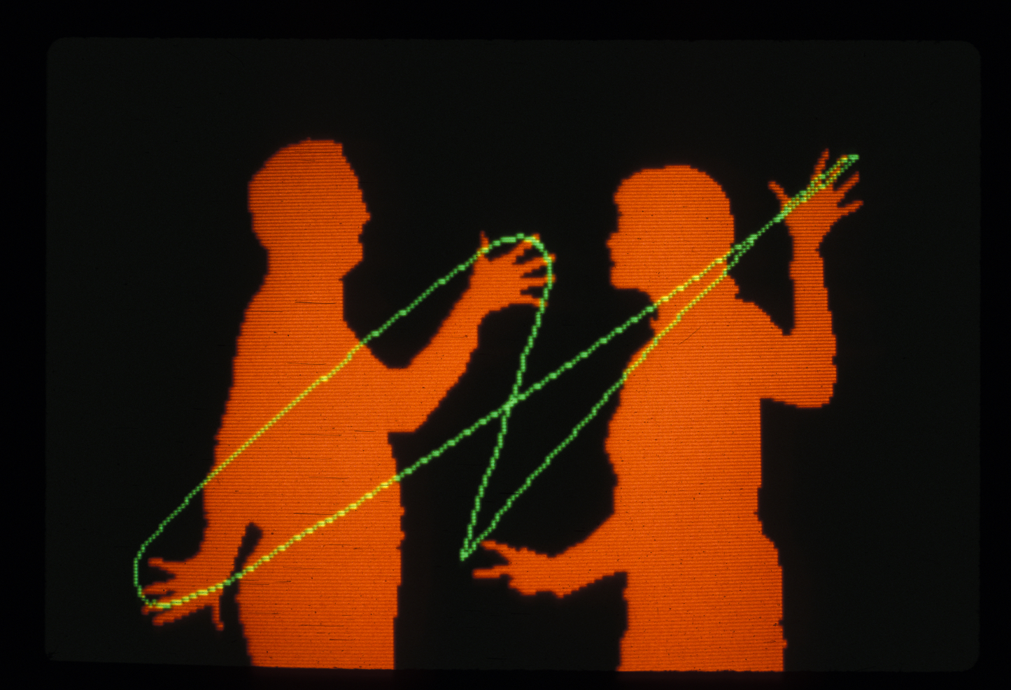 A Videoplace screen: two participants rendered as orange silhouettes against black, a green line drawn between their hands looping and stretching as they move.